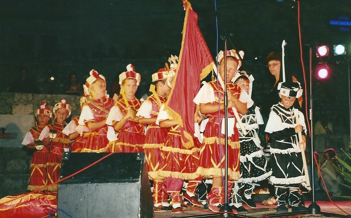 Young moreška dancers in red and black costumes on the festival stage