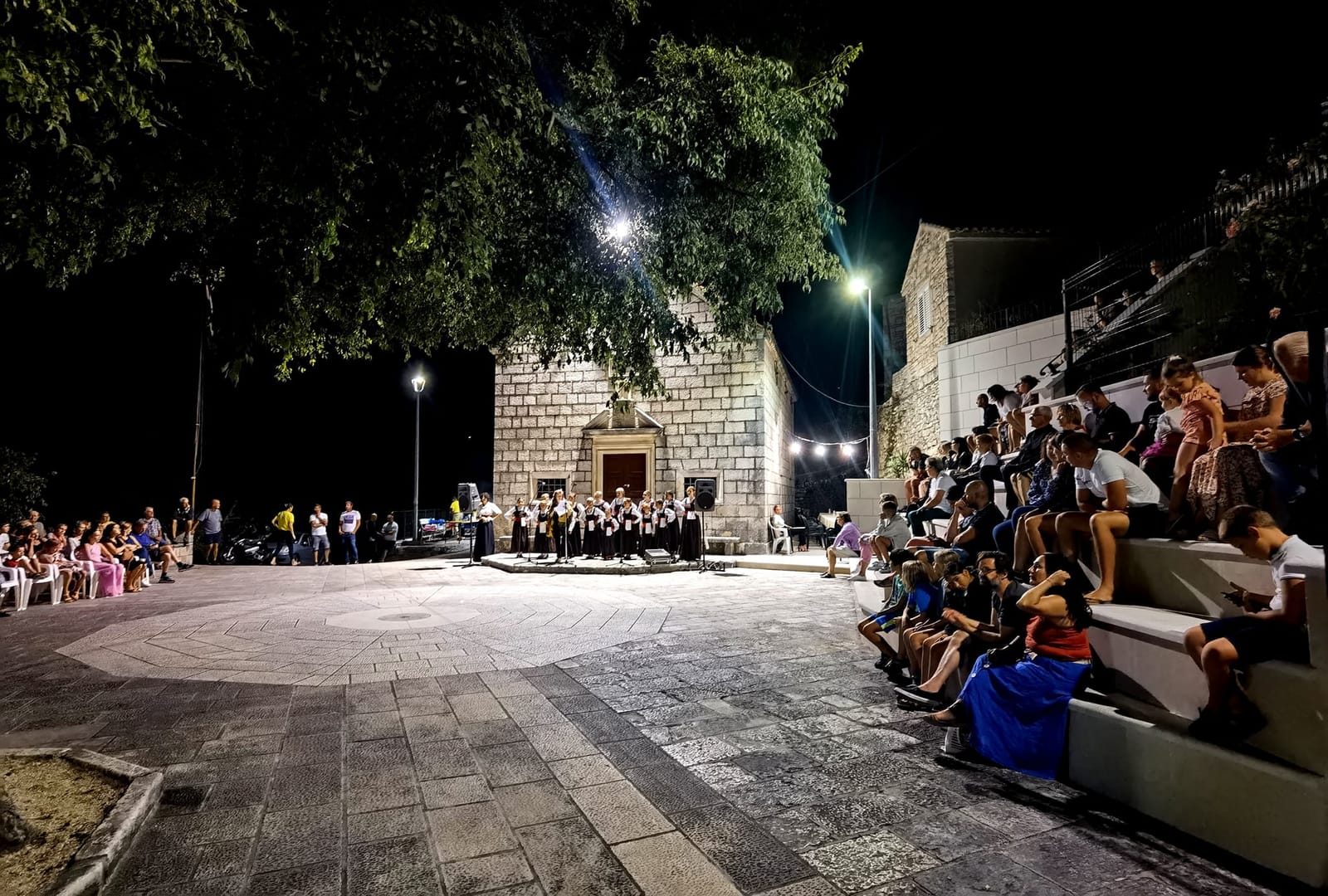 Klapa pjeva pred crkvom, publika na kamenim stubama