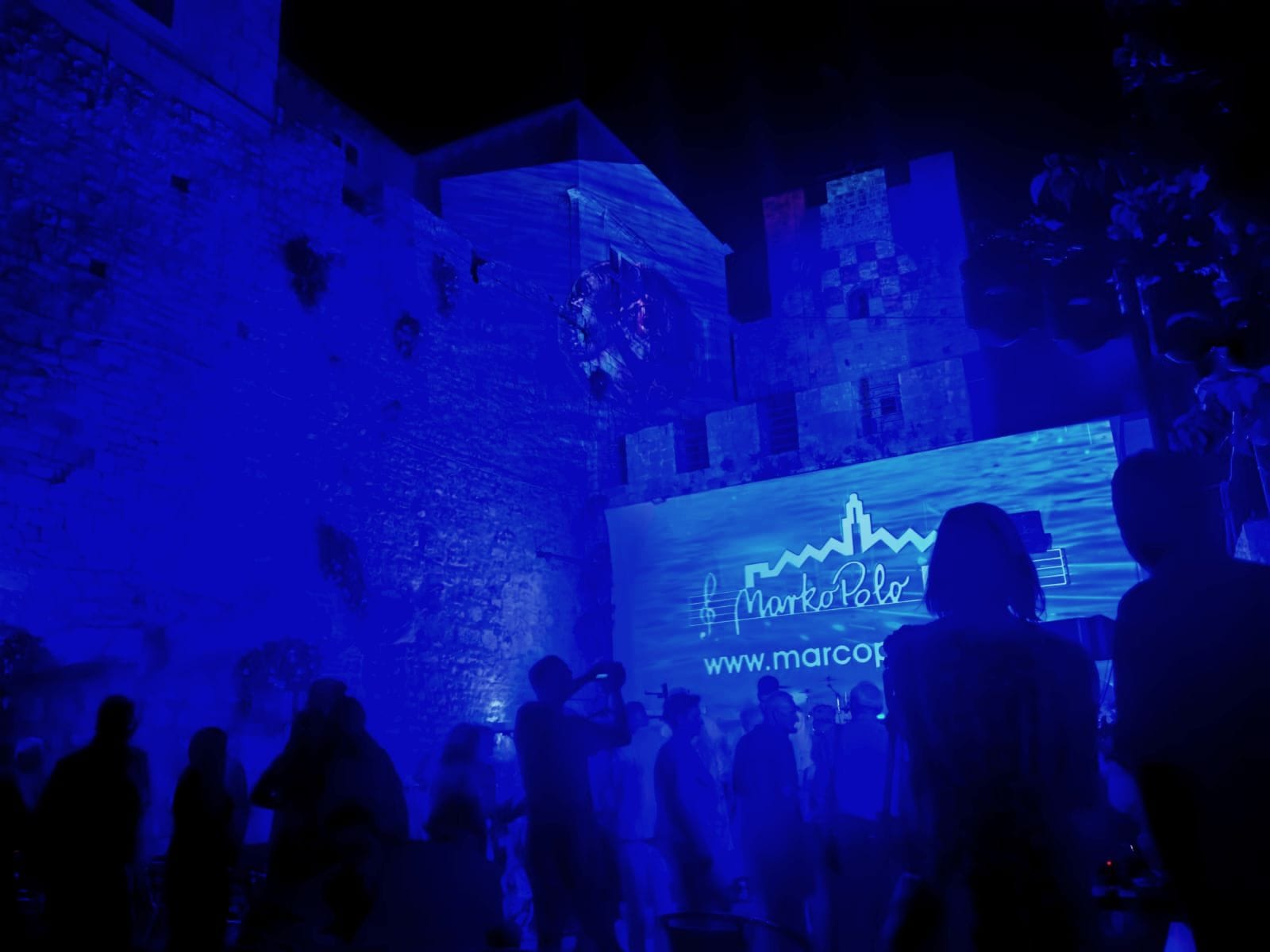 Audience beneath the illuminated town walls at an evening festival concert